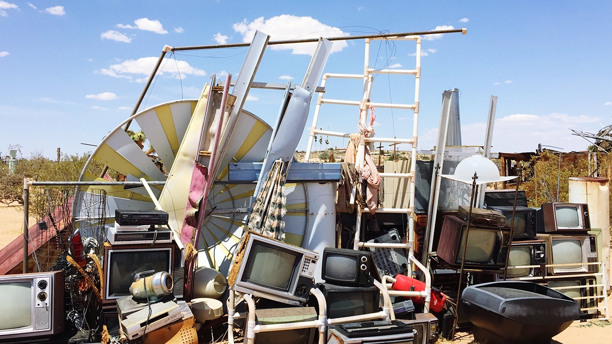 A large pile of discarded electronic waste, including old televisions and computer monitors, lies in an outdoor setting. The backdrop of a clear blue sky and sparse vegetation highlights the impact of e-waste on Hyderabad’s environment, emphasizing the challenges of managing electronic waste in the city.